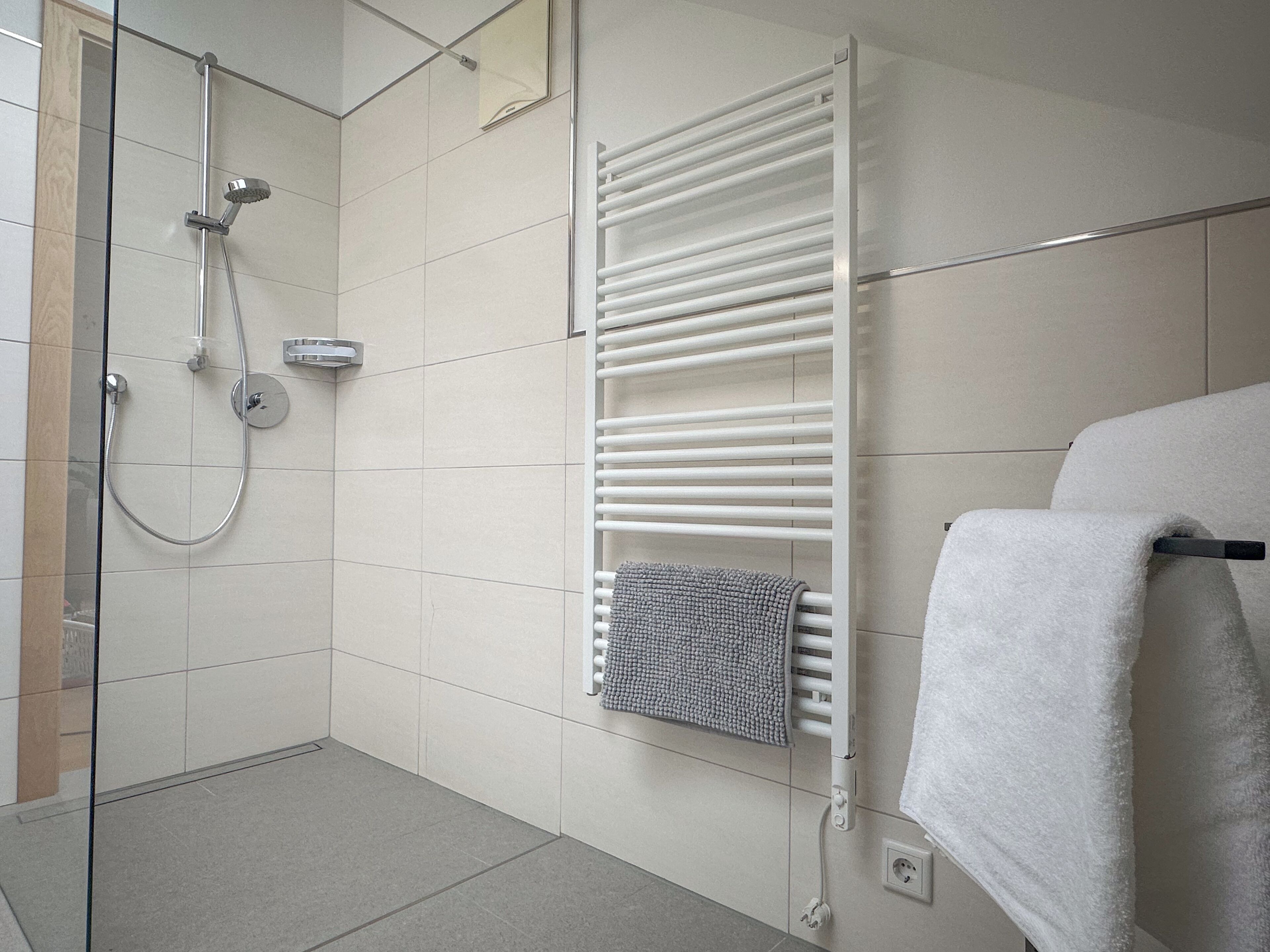 Un baño moderno con mampara de vidrio, un perchero con una toalla doblada y una toalla blanca en un perchero.