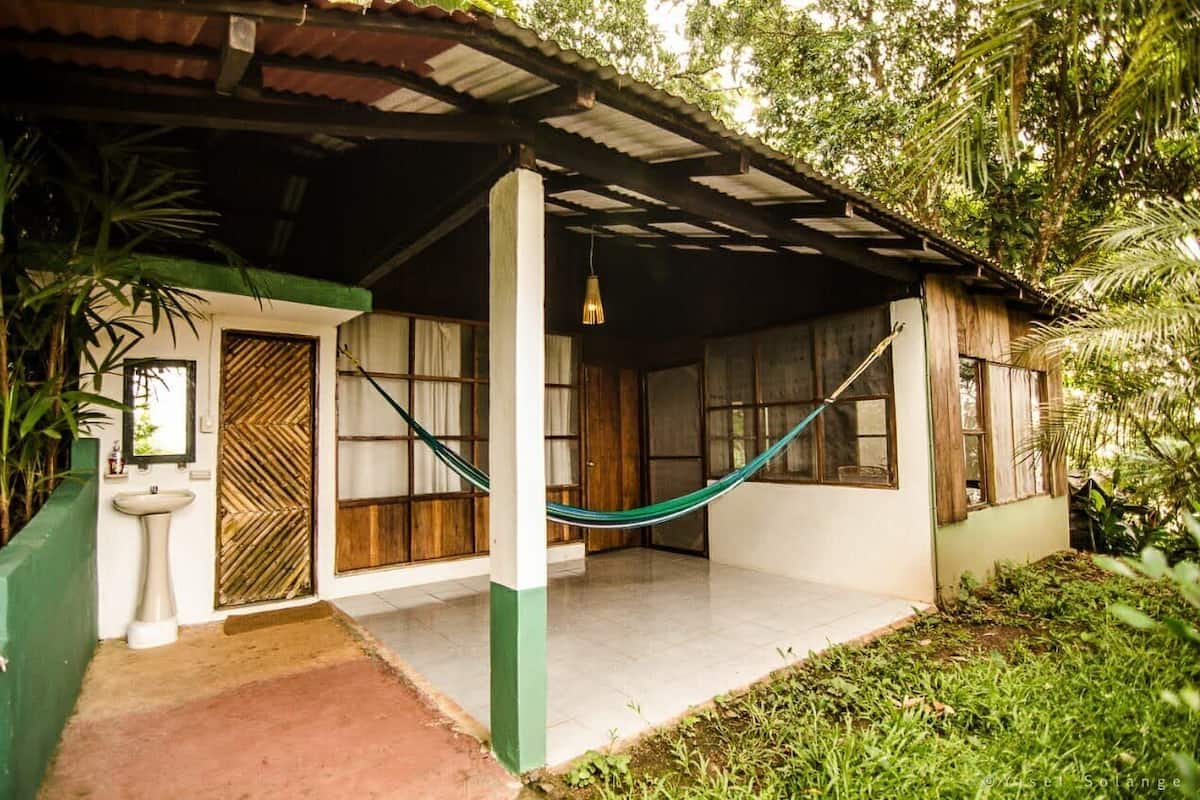 Uma casa rústica com varanda de telhado, uma rede e uma porta de madeira.