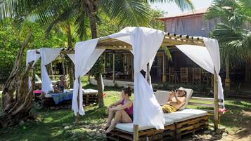 Relax in a serene garden setting with two elevated beds under canopies, surrounded by lush palm trees and a wooden structure.