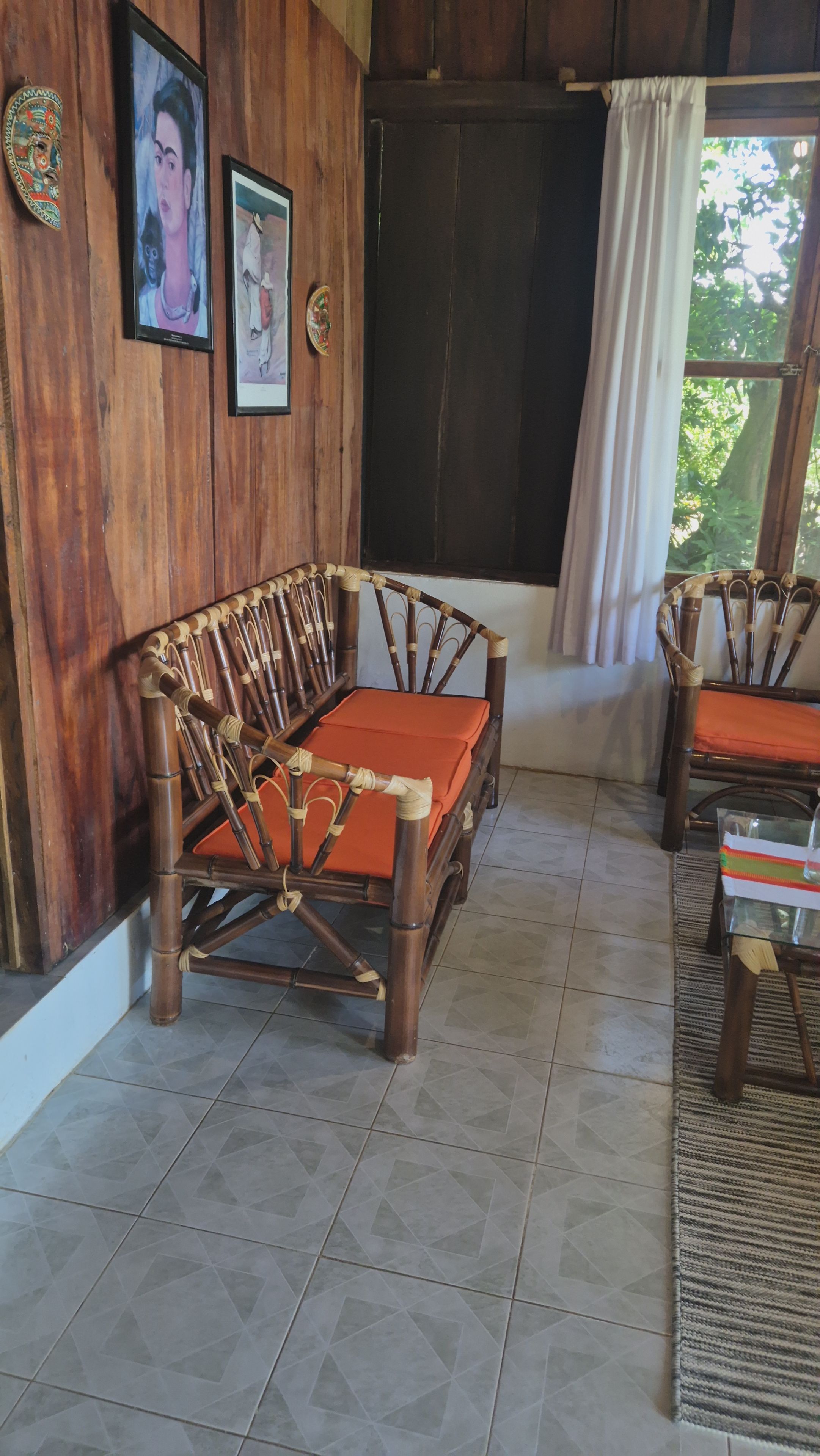 A room with a wooden wall, a sofa, a table, and a window with curtains.