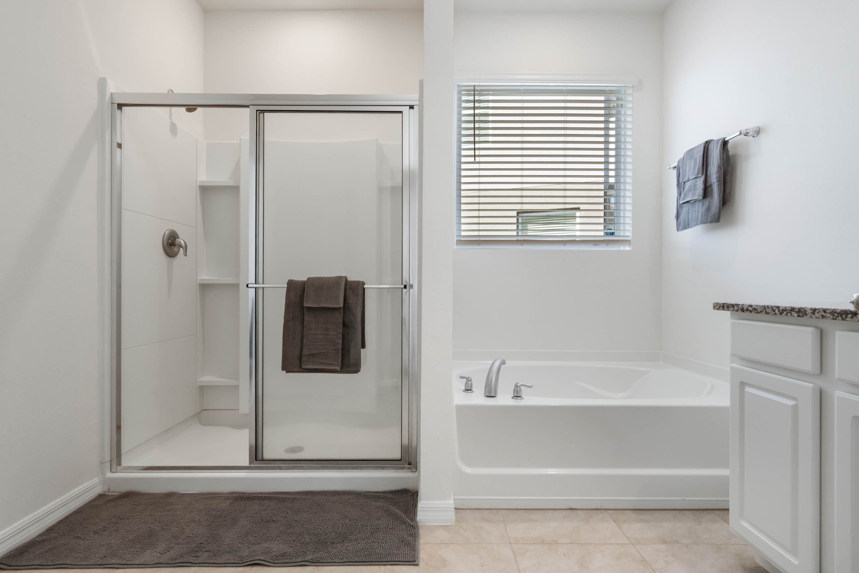 Une salle de bain moderne avec une douche à parois de verre, une baignoire sur pieds et une fenêtre équipée de stores.
