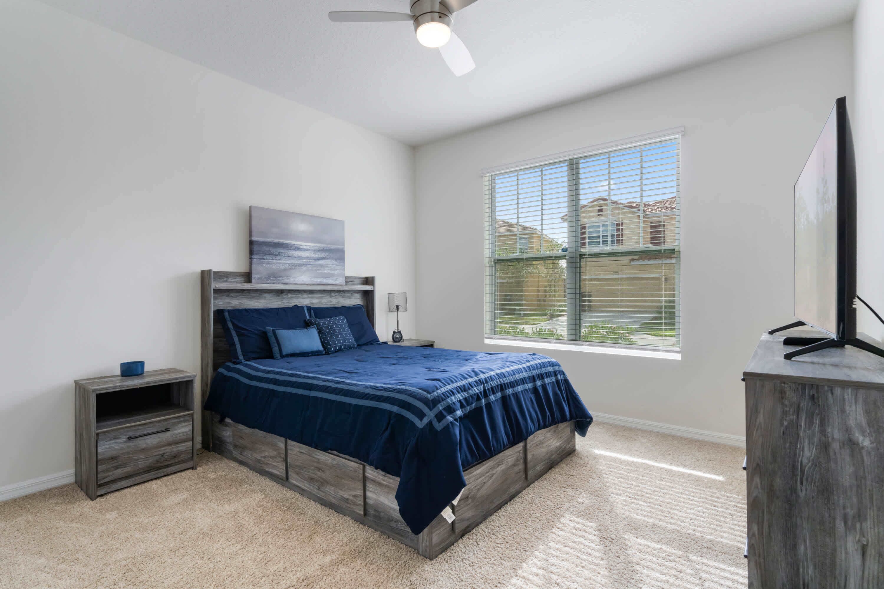 A bedroom with a bed, a nightstand, a dresser, a ceiling fan, and a window.