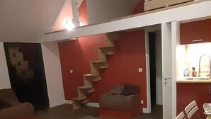 Een klein woongedeelte met een trap naar een slaapvide, een eettafel met stoelen en een kitchenette.