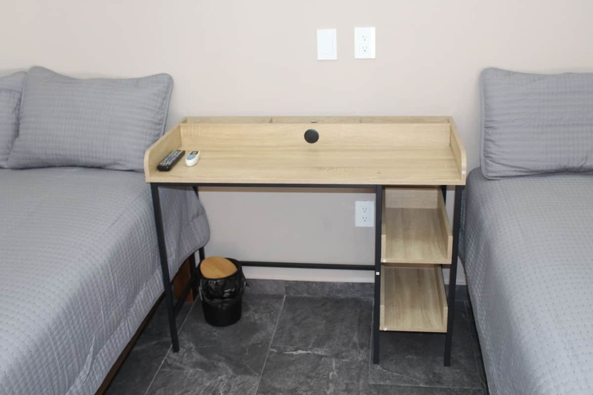 Une petite pièce avec deux lits, un bureau en bois et une poubelle.