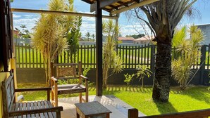 Eine überdachte Terrasse mit Holzmöbeln, gefliestem Boden und Blick auf einen grünen Garten mit Zaun und Bäumen.