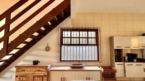 Eine geräumige Küche mit einer Holztreppe, einem großen Fenster und einem Fliesenboden.