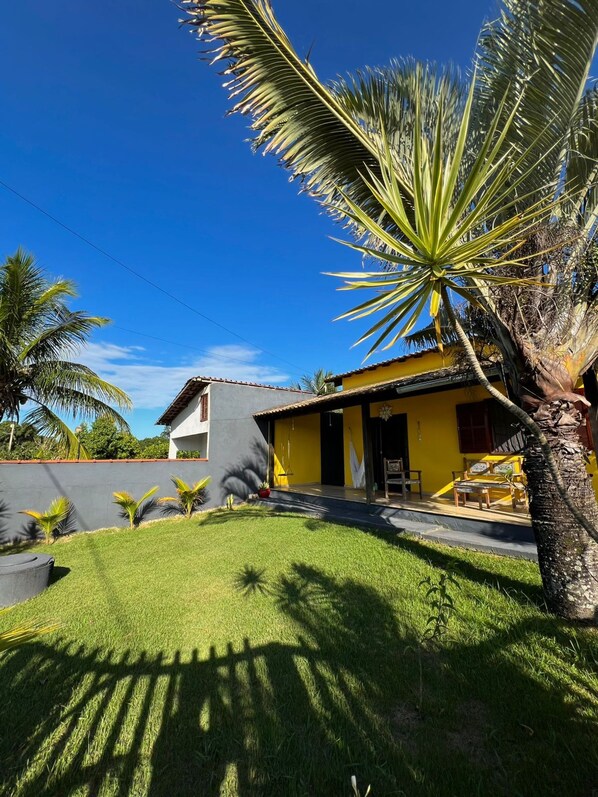 A two-story house with a yellow facade, a small porch with outdoor furniture, and a well-maintained lawn. - (Iguaba Grande)