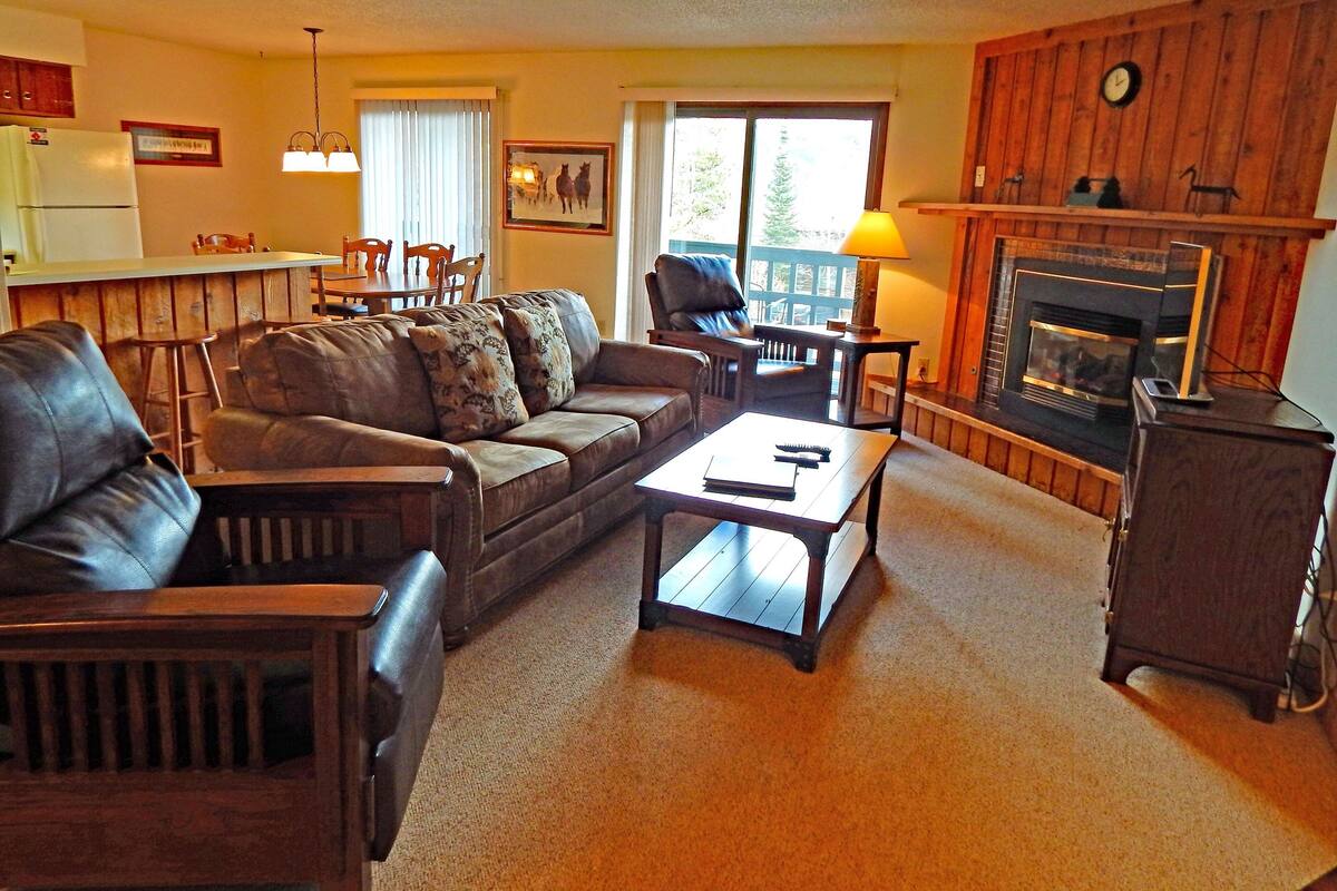 A cozy living room with a leather sofa, a wooden coffee table, and a fireplace.
