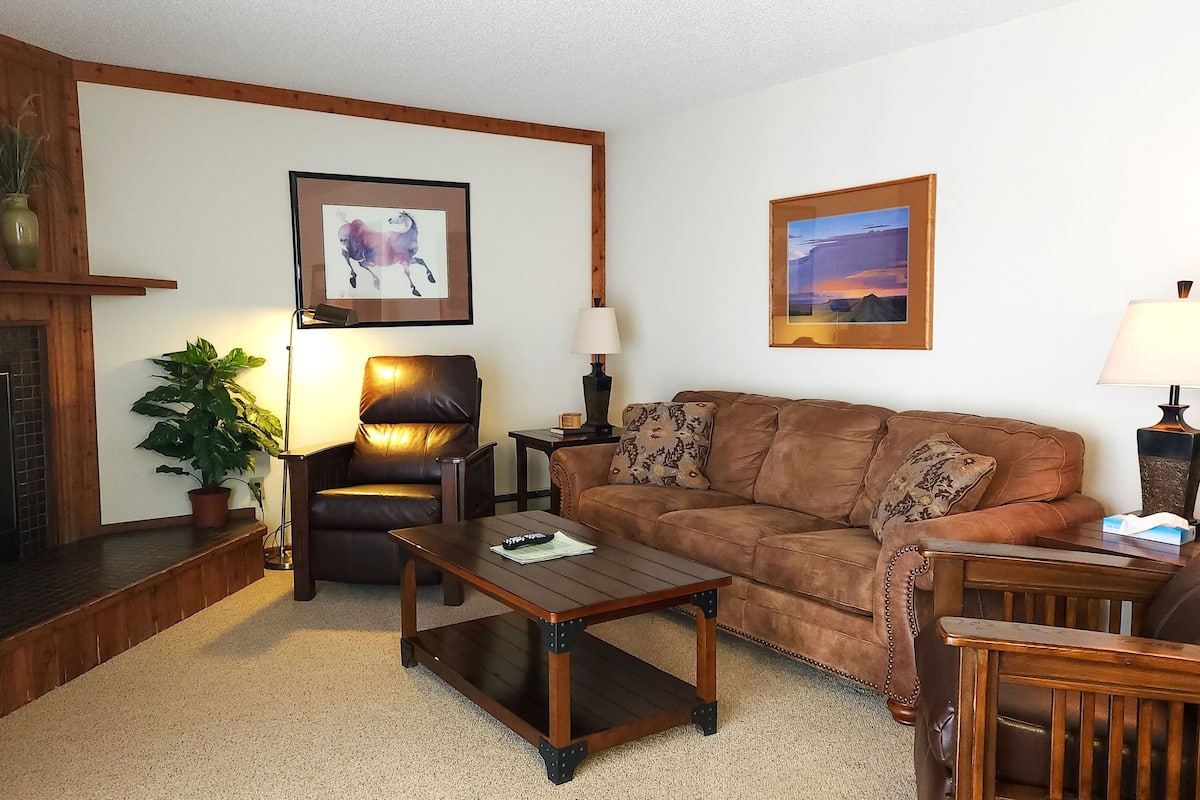 A living room with a fireplace, a sofa, a coffee table, a chair, and two lamps.