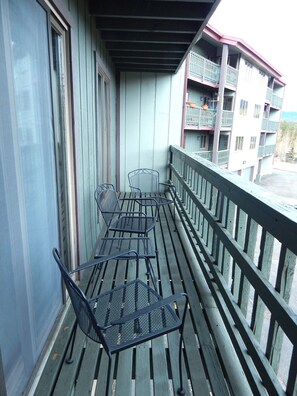 A balcony with metal chairs and a table, wooden railings, and a view of a multi-story building with balconies.