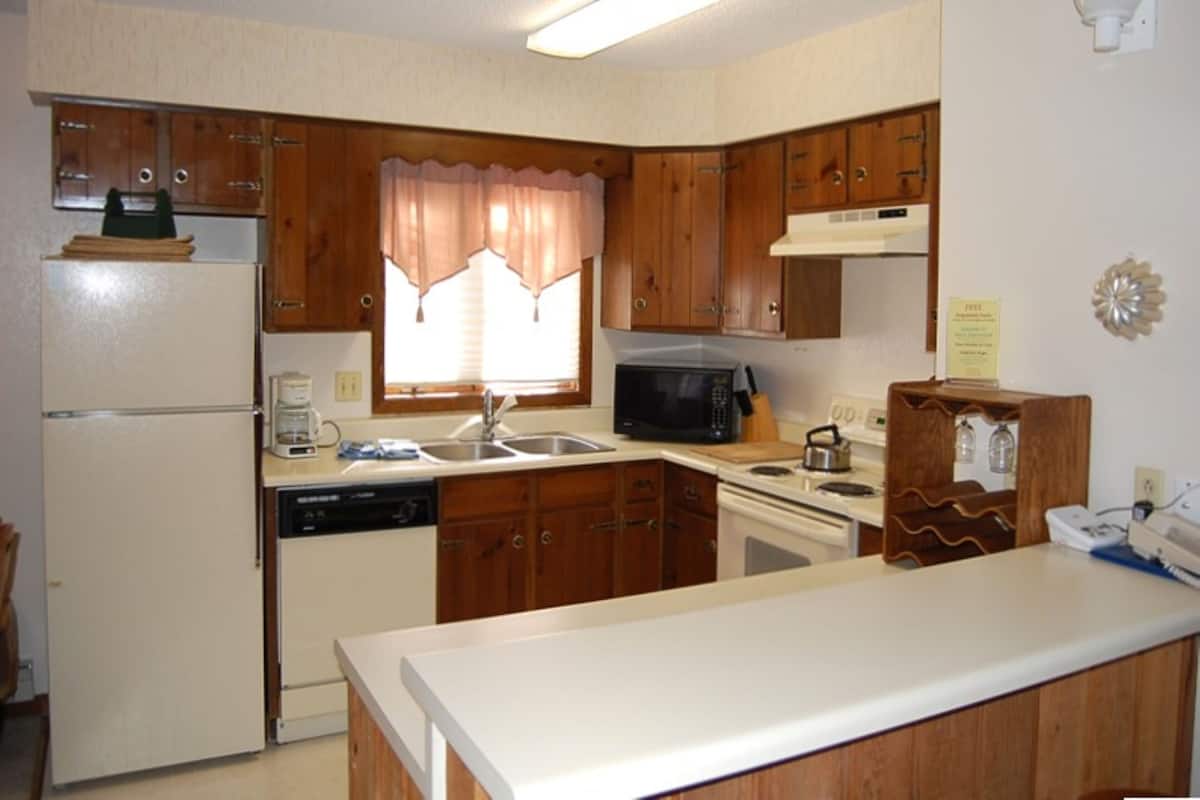A compact kitchen with wooden cabinets, a refrigerator, a microwave, a sink, and a stove.