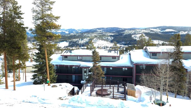 A snow-covered building with multiple windows and a fenced outdoor area. - Timber Run (Winter Park)