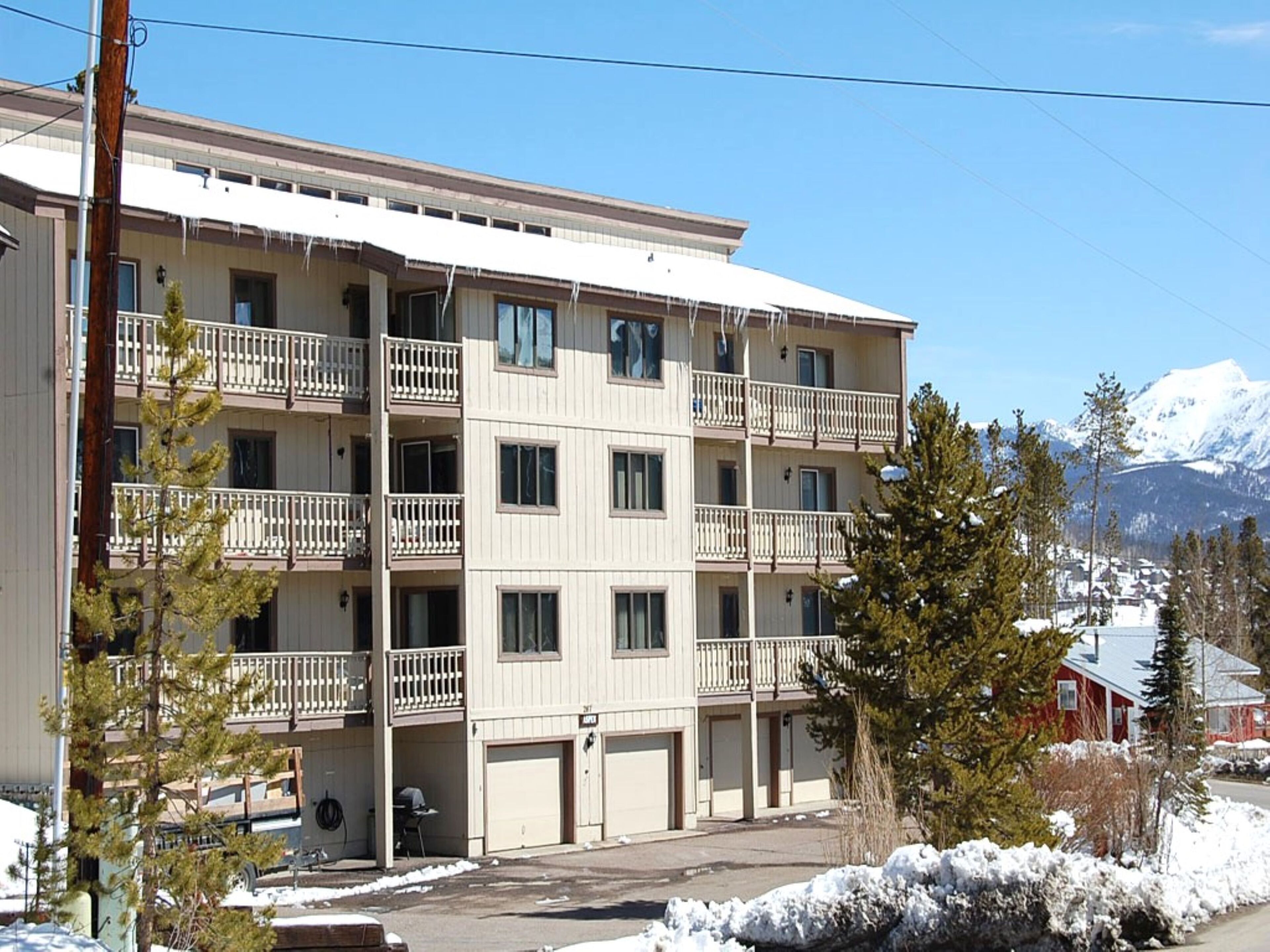 A multi-story hotel with balconies, a parking area, and a view of snow-capped mountains.