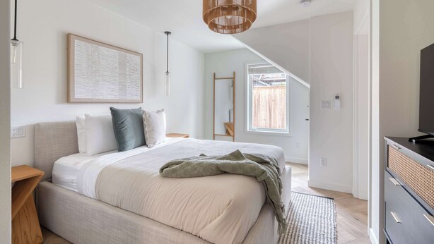 Une chambre avec un grand lit, une table de chevet en bois, un luminaire suspendu et un tableau encadré au mur.