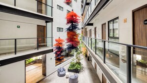 Un couloir d’hôtel moderne avec des rampes de protection en verre, une colonne centrale ornée de motifs colorés et dynamiques, et des plantes en pot.