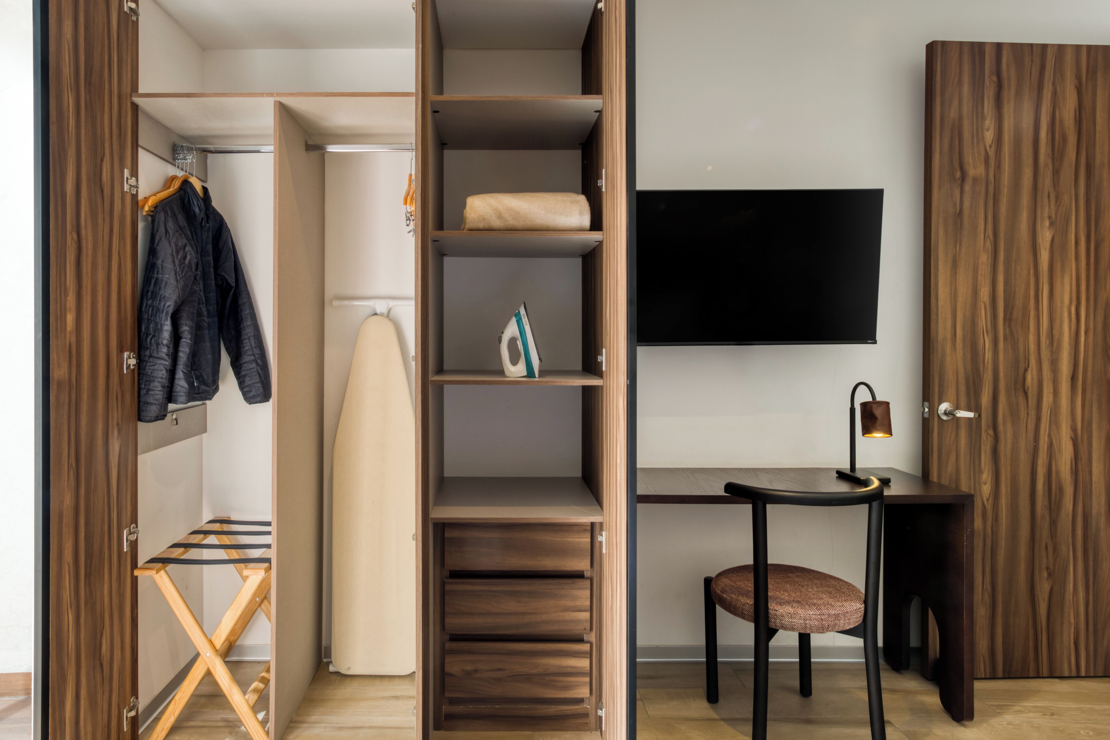Una habitación moderna con un armario de madera, un escritorio con silla y una percha con ropa.