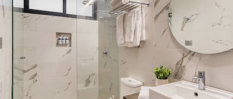 A modern bathroom with a glass-enclosed shower, a white toilet, a sink with a mirror, and a marble-tiled wall.