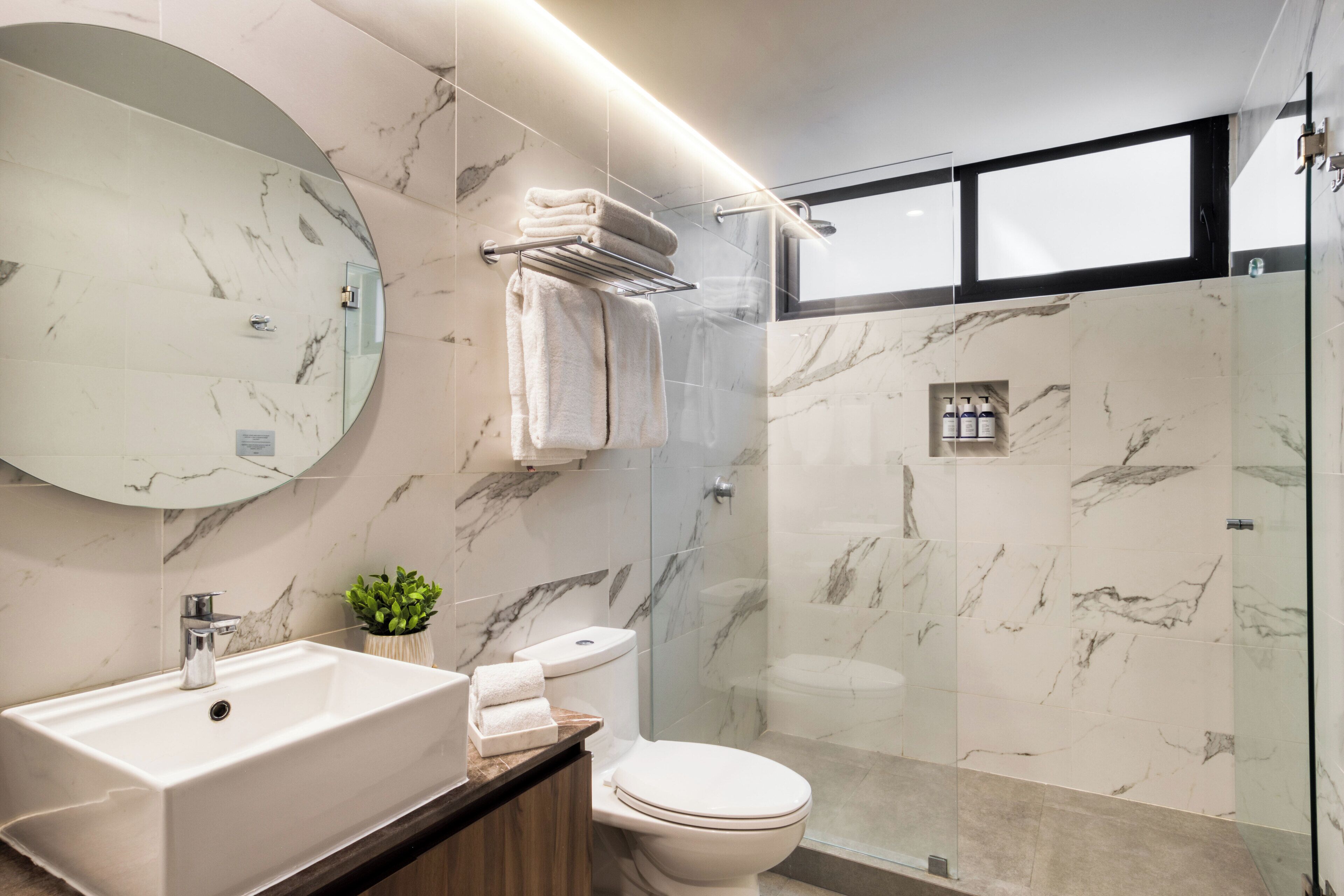 A modern bathroom with a marble sink, a toilet, and a glass-enclosed shower area.
