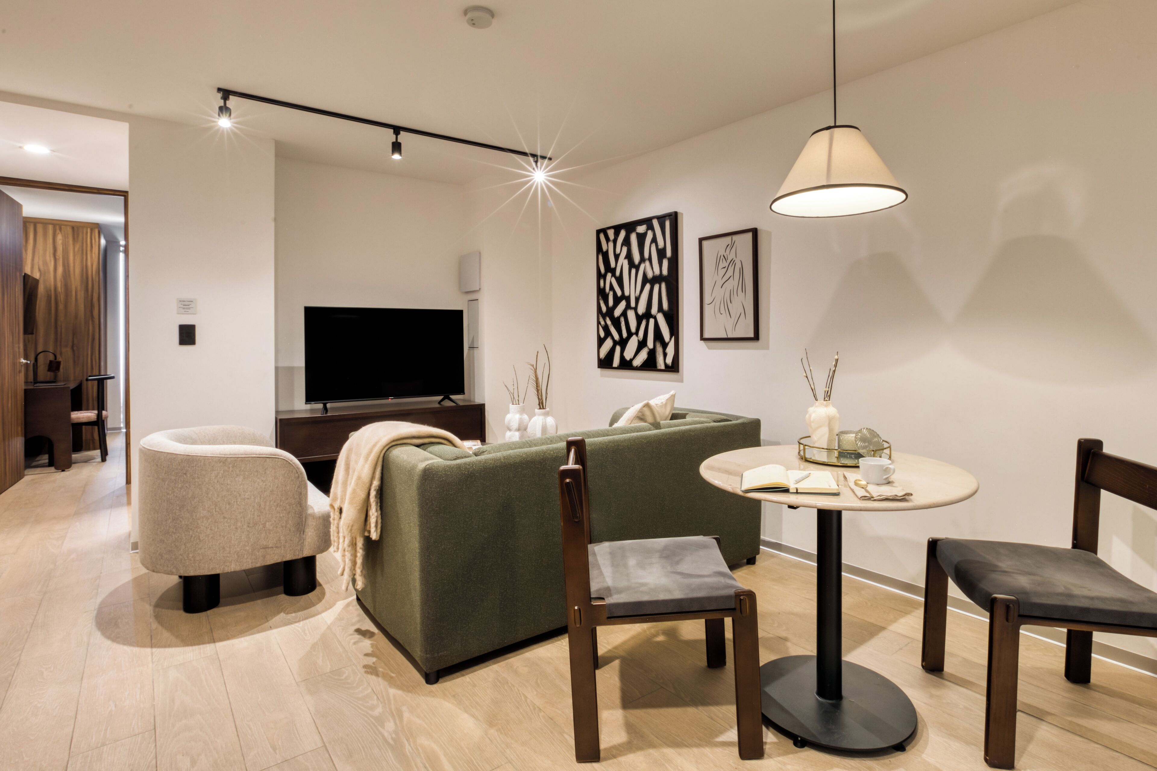 A modern living room with a sofa, two chairs, a round table, a flat-screen TV, and decorative wall art.