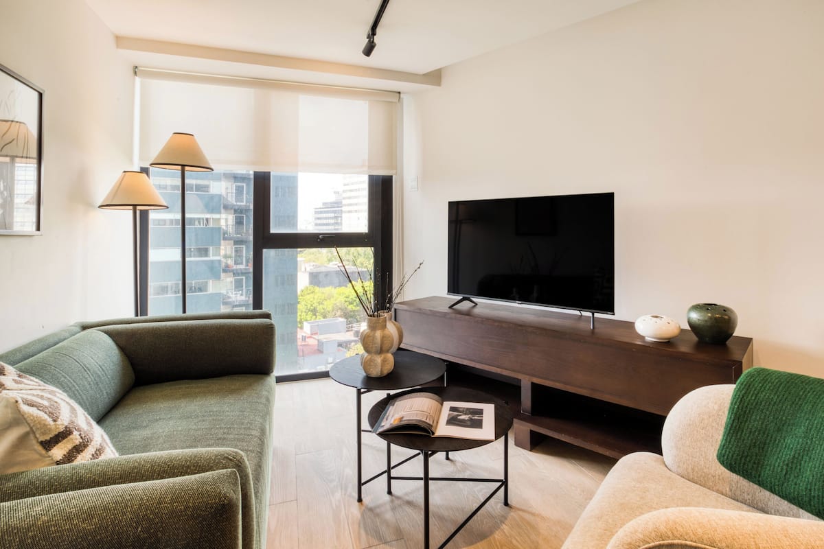 Ein modernes Wohnzimmer mit einer Couch, einem Couchtisch, einem Fernseher und einem großen Fenster mit Blick auf die Stadt.
