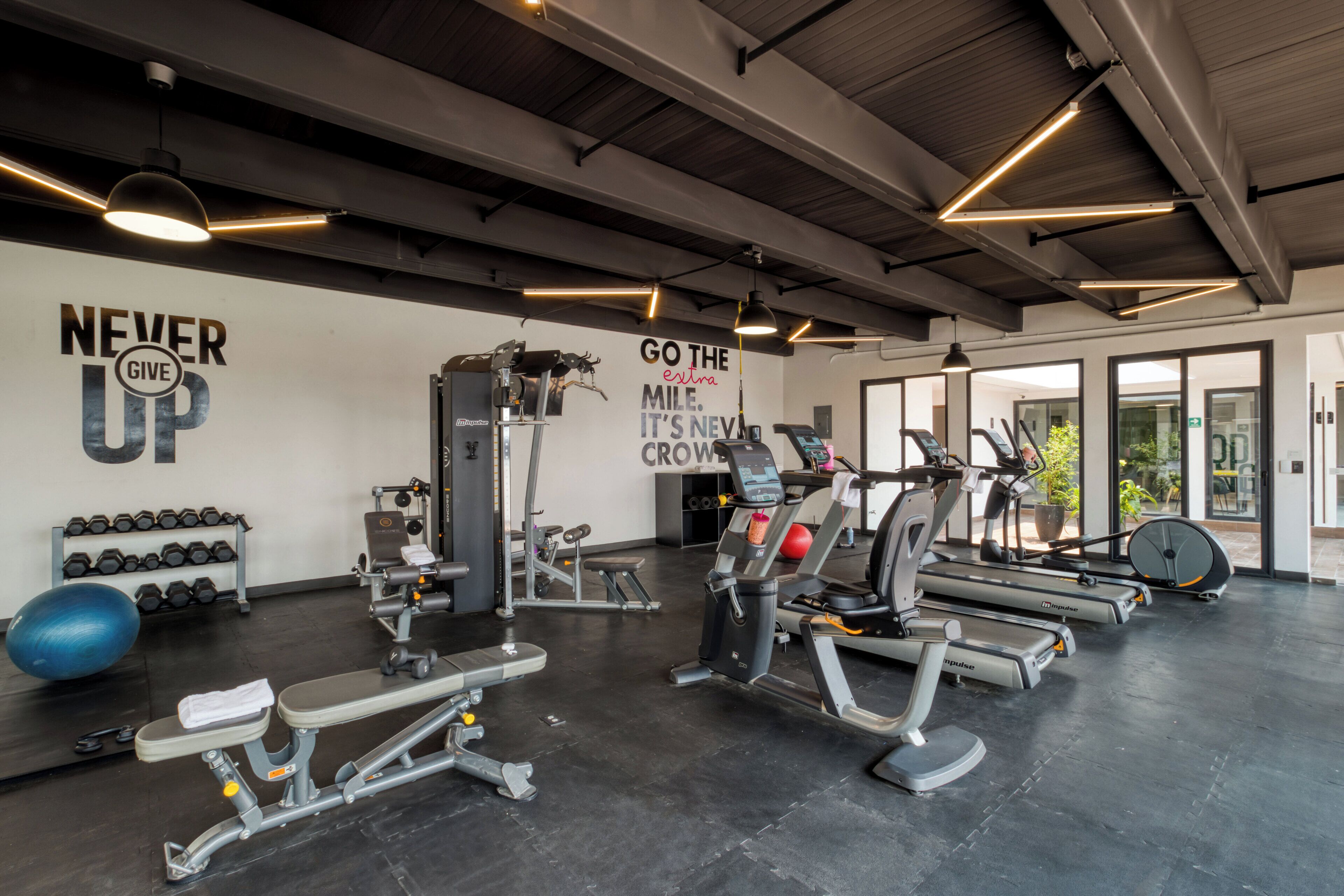 A gym with various exercise equipment, motivational wall quotes, and a rack of dumbbells.