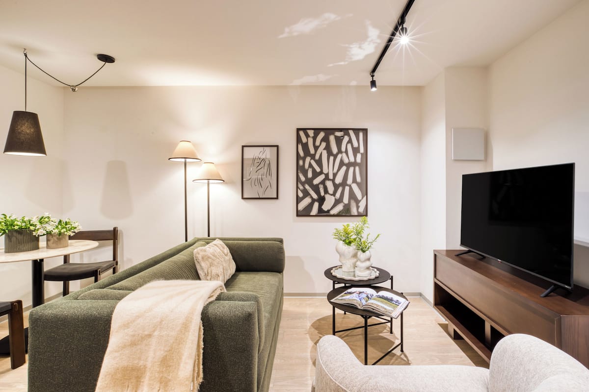 Ein modernes Wohnzimmer mit Sofa, Couchtisch, Fernseher und einem Essbereich mit Stühlen und Tisch.