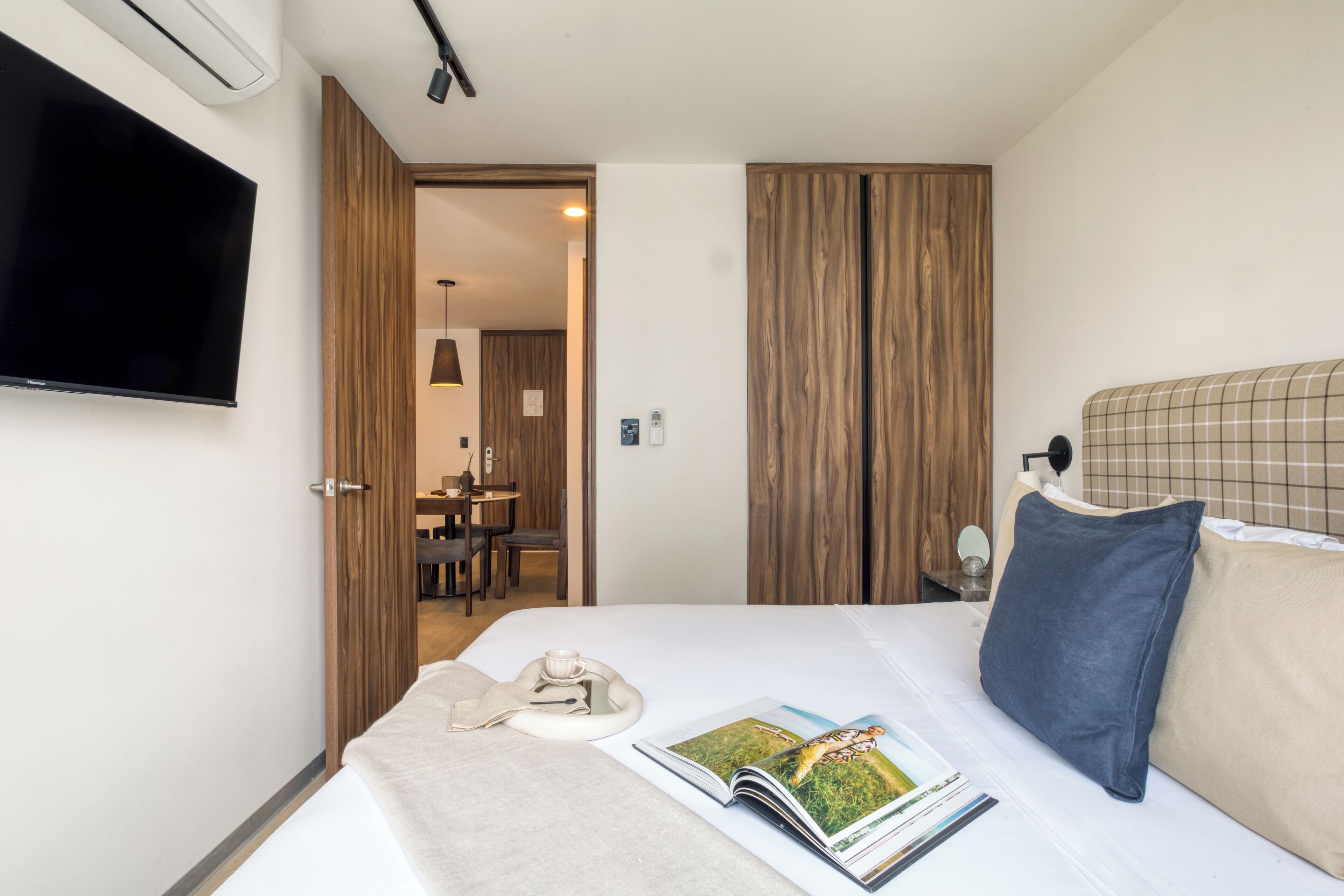 Habitación de hotel con cama, televisor de pantalla plana en la pared, zona de comedor con mesa y sillas, y paneles de madera en las paredes.
