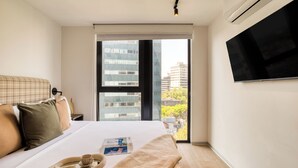 Une chambre d’hôtel moderne avec un grand lit, un téléviseur à écran plat fixé au mur et une vue sur la ville par la fenêtre.