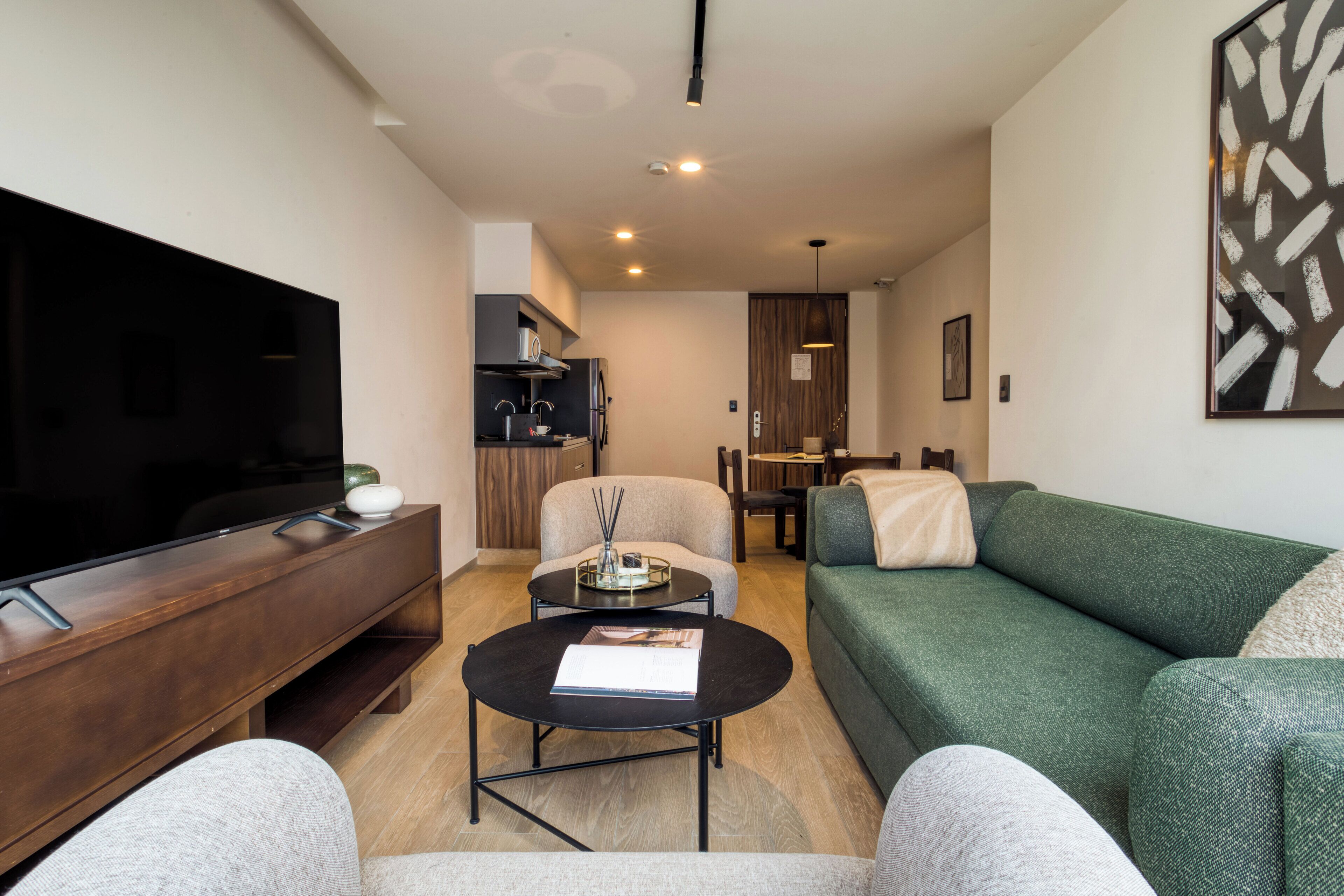 Ein modernes Wohnzimmer mit Flachbildfernseher, Couchtisch, Sofa und einem Essbereich im Hintergrund.