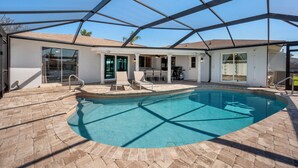 A swimming pool with a glass enclosure, surrounded by a patio area with chairs and a table. - Summer Sale! 6 min to Downtown-Waterfront, Heated Pool, Beach Essentials (Cape Coral)