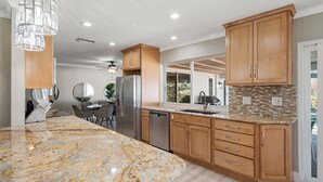 A modern kitchen with granite countertops, wooden cabinets, and a large island. - Summer Sale! 6 min to Downtown-Waterfront, Heated Pool, Beach Essentials (Cape Coral)