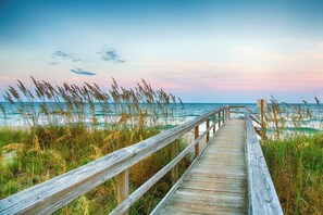A wooden boardwalk leading to the beach with tall grasses and a clear sky.