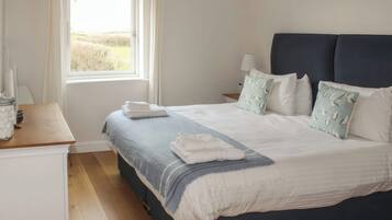 A neatly made bed with pillows and a blanket, a bedside table with a lamp, and a window with curtains.