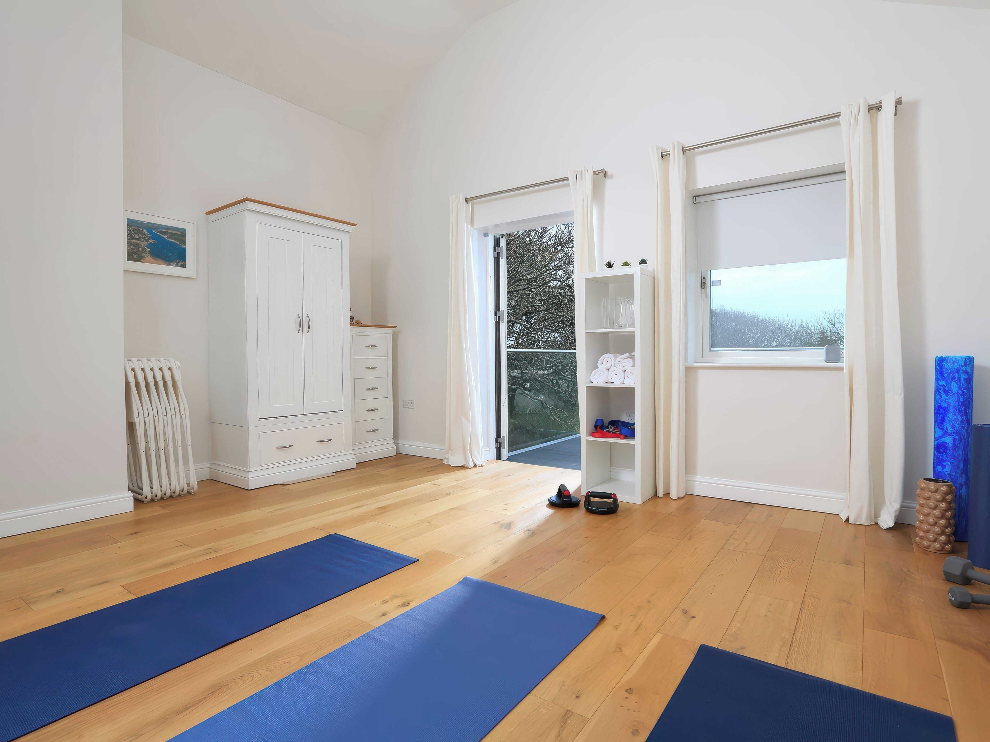 A room with wooden flooring, a white wardrobe, a radiator, a door leading outside, and blue exercise mats.