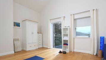 A room with wooden flooring, a white wardrobe, a radiator, a door leading outside, and blue exercise mats.