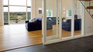 A spacious living area with a large glass door leading to a balcony, a dark blue sofa, and a wooden floor. - Moult Hill Barn (Salcombe)