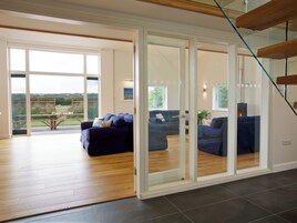 Amplia sala de estar con un gran ventanal que da a un balcón, un sofá azul oscuro y piso de madera.