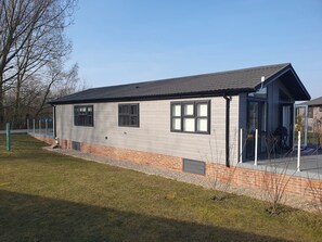 A single-story building with a flat roof, large windows, and a brick base. - 2-bed Lodge, Sleeps 5 w/ Hot Tub & Lake View (Beverley)