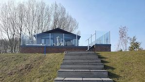 A modern building with a glass facade, a brick base, and a set of stone steps leading to a glass railing. - 2-bed Lodge, Sleeps 5 w/ Hot Tub & Lake View (Beverley)