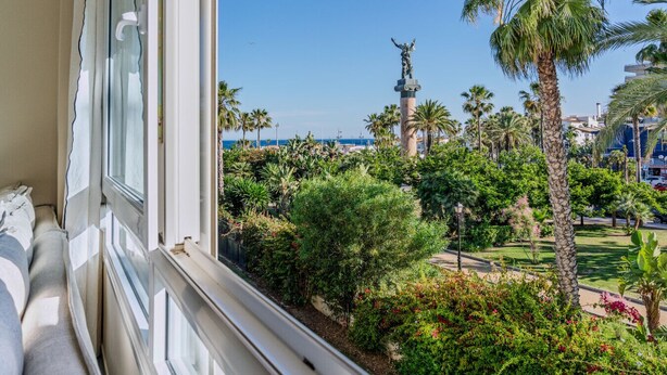 A balcony with a view of a landscaped garden, palm trees, and a statue. - Front Line Playa Rocio P. Banus (Marbella)