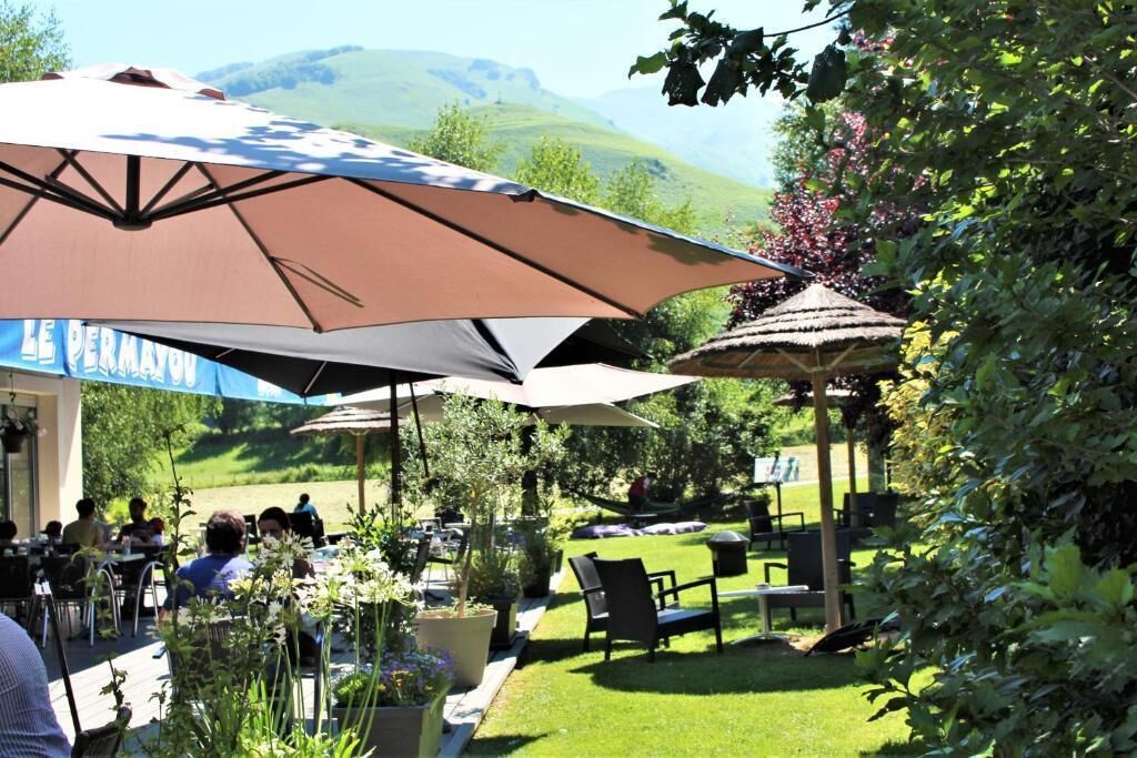 An outdoor dining area with tables and chairs, umbrellas, and a view of a hilly landscape.