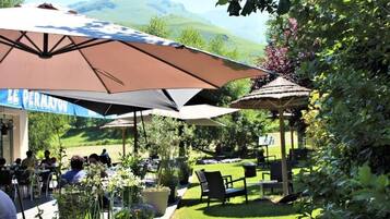 An outdoor dining area with tables and chairs, umbrellas, and a view of a hilly landscape.