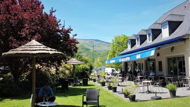 An outdoor cafe area with tables and chairs, a thatched umbrella, and a building with a blue awning.