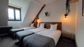 A bedroom with two beds, a sloped ceiling, and a window.