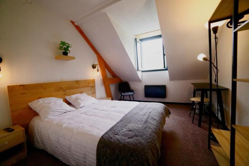 A bedroom with a wooden headboard, a bed with white bedding, a small table with two chairs, a TV, and a window with a view.
