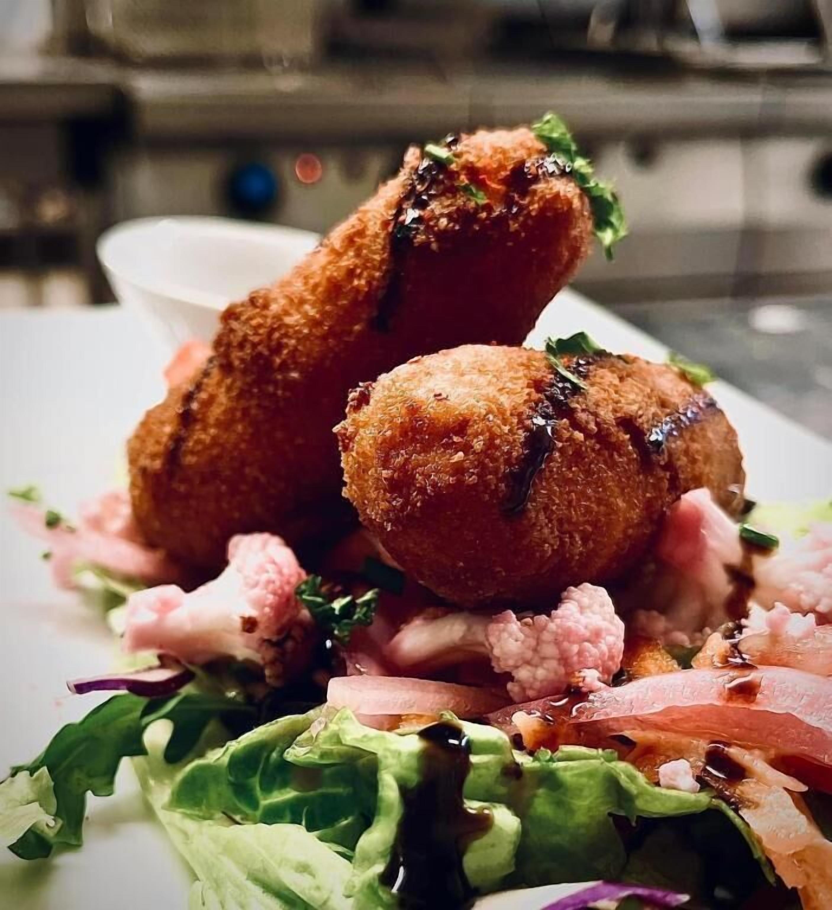 Een bord met gepaneerde en gefrituurde snacks, mogelijk kroketten, geserveerd met een salade.