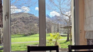 A dining table with cutlery and a glass, set against a window with a view of a mountainous landscape.