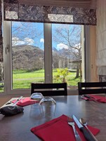 A dining table with cutlery and a glass, set against a window with a view of a mountainous landscape.