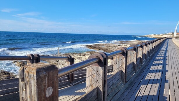 A wooden boardwalk leading to a rocky shoreline with waves crashing onto the beach.