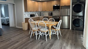 A compact kitchen with wooden cabinets, a dining table with chairs, a built-in washer and dryer, and a sign reading "ME TO THE BEACH". - Charming 2-bedroom condo with WiFi, AC in amazing Ocean City (Ocean City)